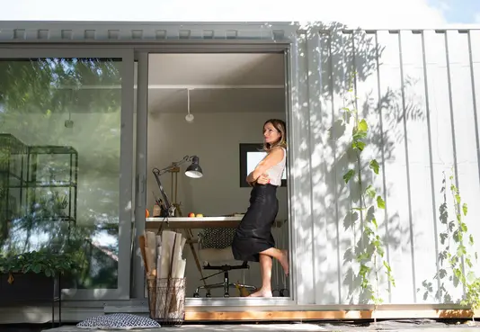 Modulhaus-Containerhaus-Eigenheim Frau steht Barfuss in einer Tür ihres Arbeitscontainers